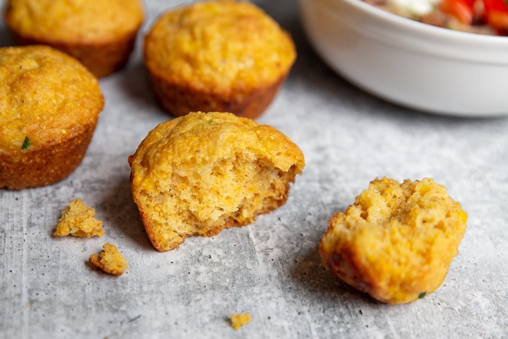 A jalapeno cornbread muffin on a counter top, with a bowl of chili in the background.