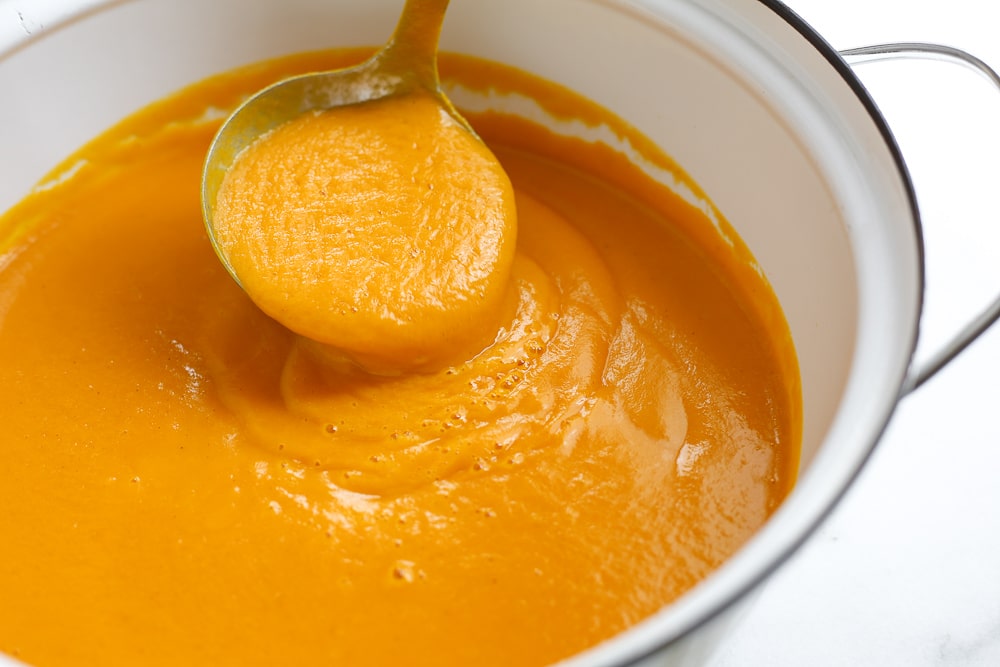 Close up of a ladle scooping the sweet potato soup out of a pot.