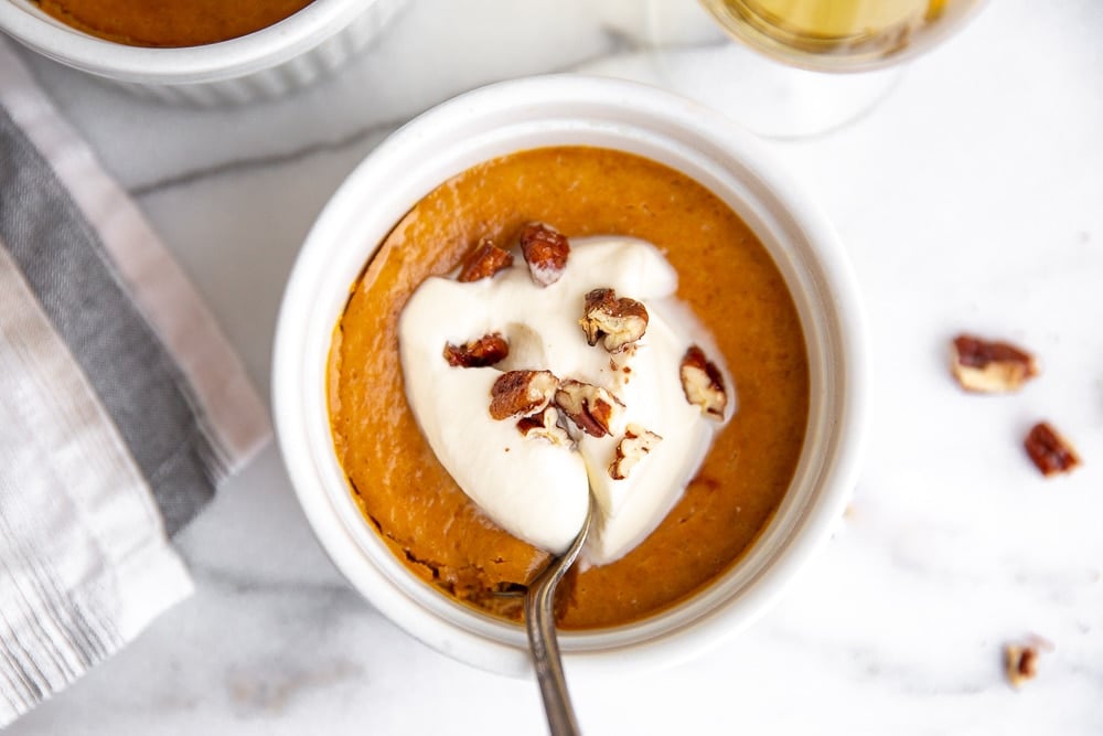 A pumpkin pie custard topped with whipped cream with a spoon. 