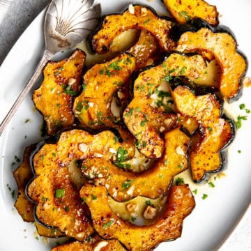 Roasted acorn squash slices on a serving platter with brown butter sauce.
