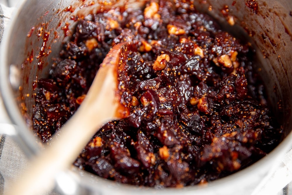 Process shot showing the finished fig chutney in pot with a wooden spoon.