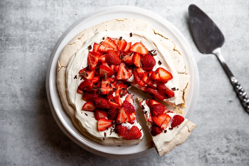 Pavlova with dark chocolate and strawberries on a cake stand with a cake server alongside.