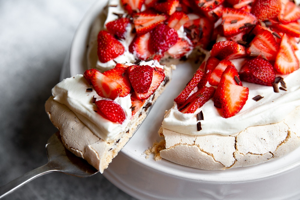 Close up of a slice of pavlova with dark chocolate, topped with whipped cream and strawberries.