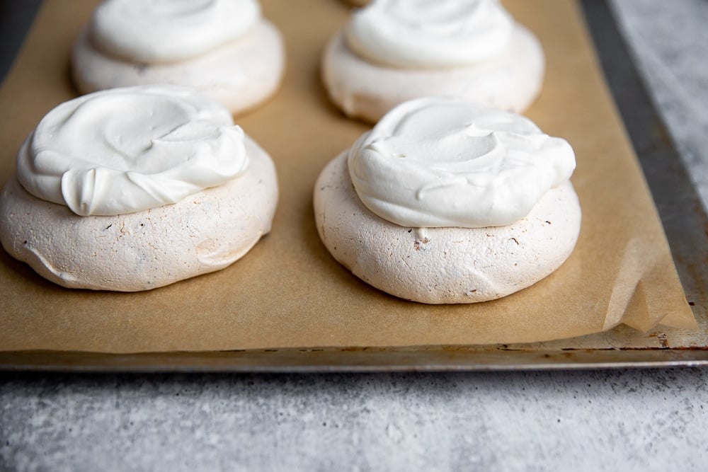 Mini pavlovas topped with whipped cream on a baking sheet.