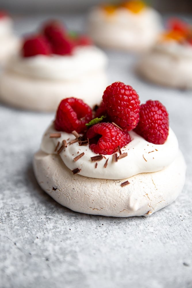 Close up side view of a mini pavlova topped with whipped cream and raspberries.