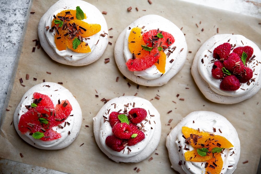 Overhead shot of mini pavlovas lined up on parchment paper. 