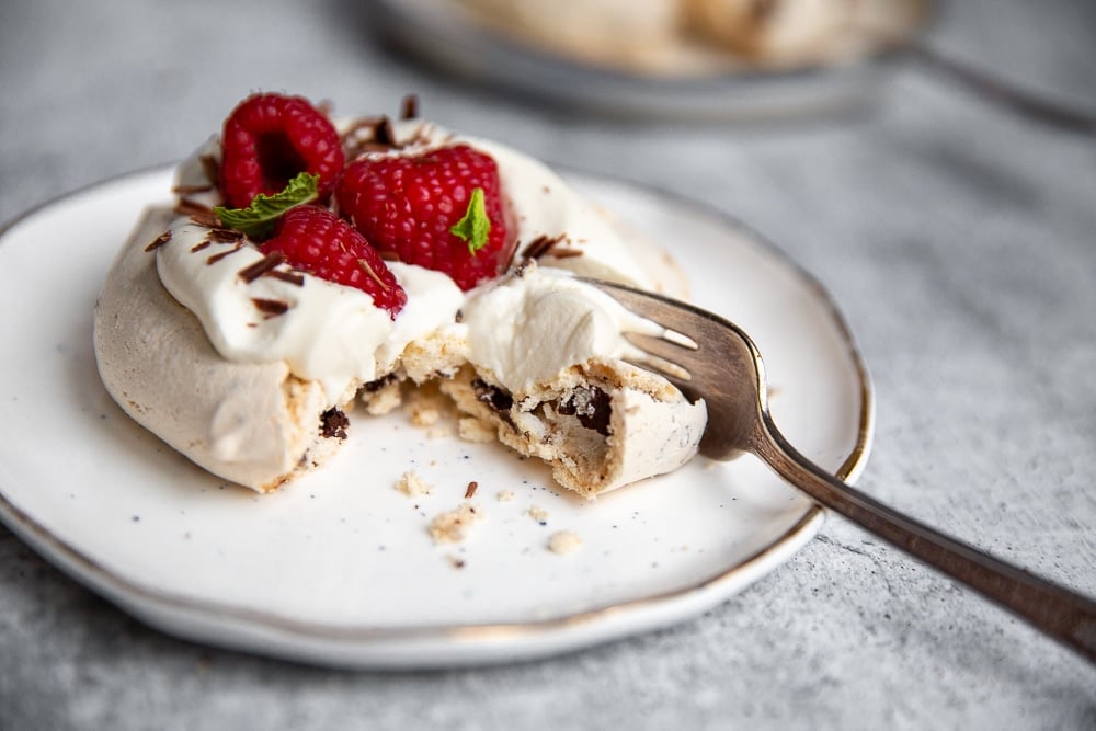 Close up of a mini pavlova on a plate with a fork taking a bite. 