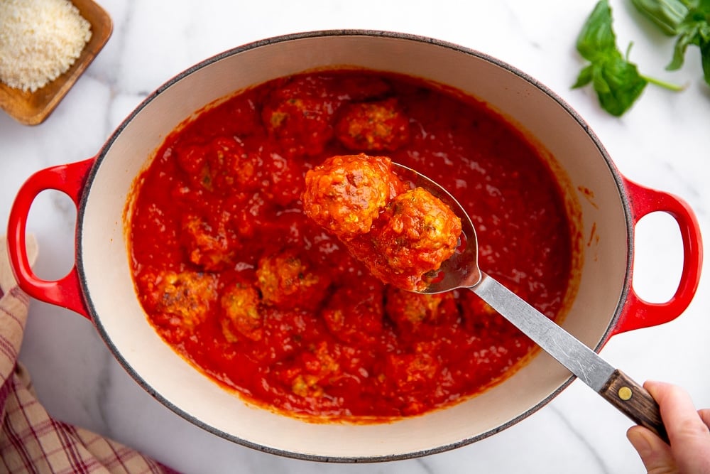 A large spoon holding two turkey meatballs in marinara sauce, with the pot in the background. 