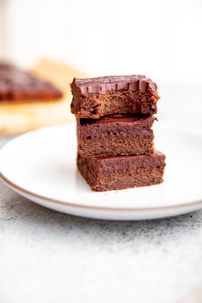 Close up of black bean brownies with cacao frosting stacked on a plate. 