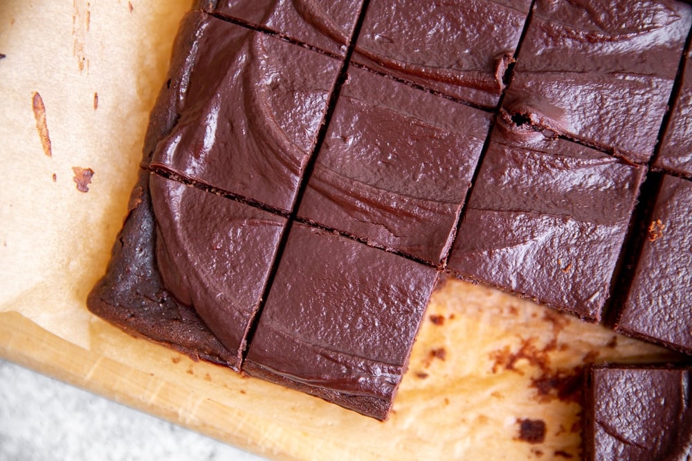 Overhead shot of black bean brownies with cacao frosting on a wooden serving board. 