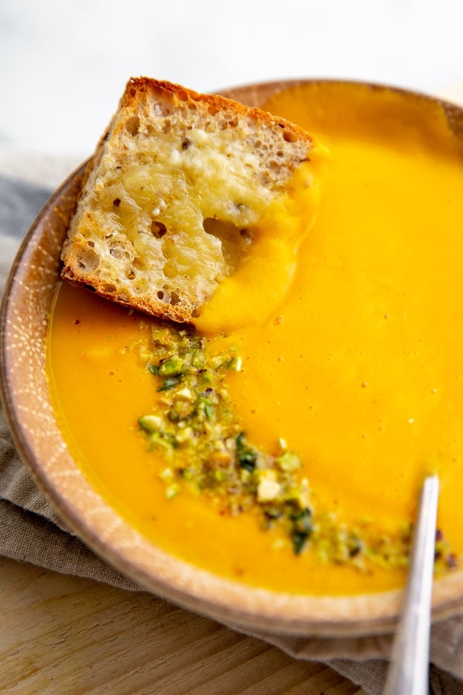 Close up of a cheesy baguette dunking into a bowl of potage soup. 