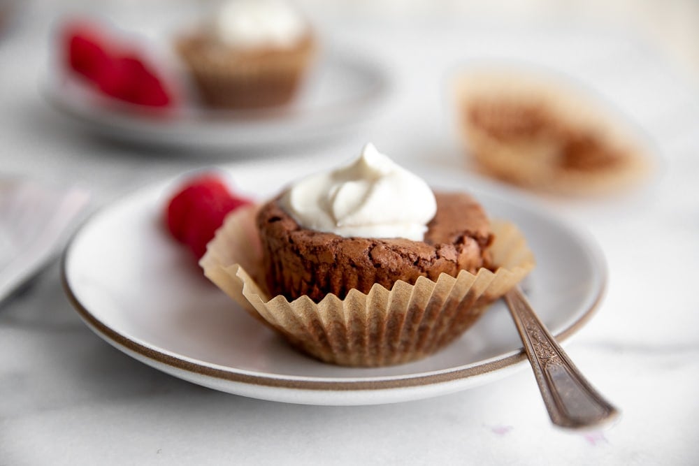 Close up of an individual chocolate cake in a muffin liner on a plate with a fork.