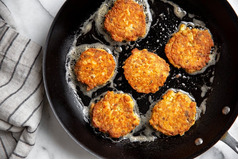 Salmon cakes cooking in a skillet. 