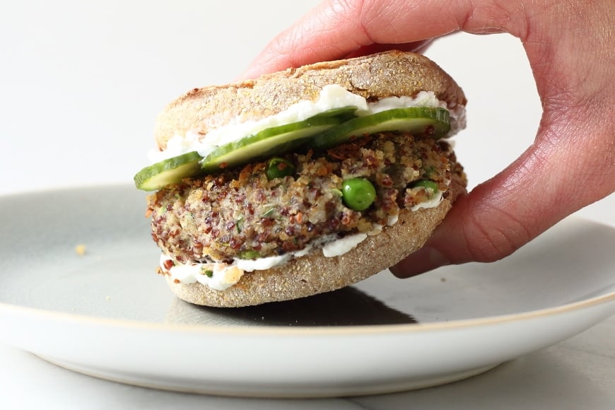 Quinoa and white bean burger on a plate with a hand grabbing it. 