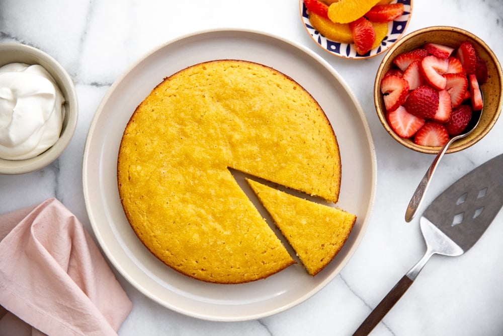 Almond cake on a plate with fruit alongside. 