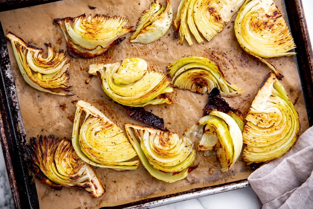 Process shot showing roasted cabbage wedges on a parchment-lined baking sheet.