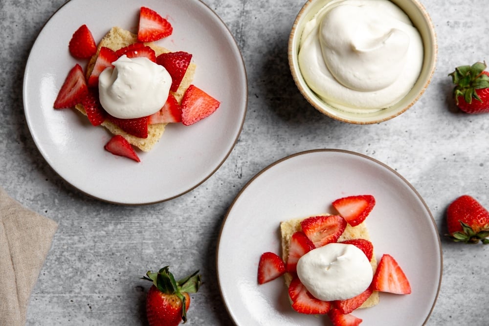 Strawberry shortcakes on plates topped with sliced strawberries and whipped cream. 