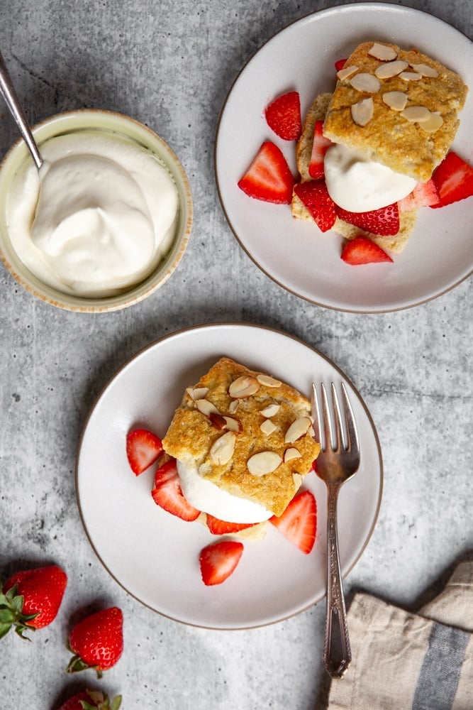 Strawberry shortcakes on plates with a bowl of whipped cream alongside. 