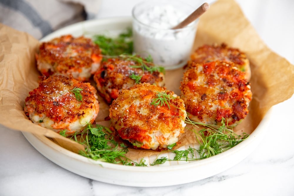 Salmon potato cakes on a serving plate with yogurt sauce in the background. 