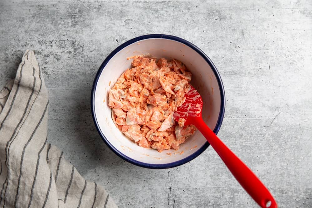 salmon salad mixed in a bowl with a red spatula