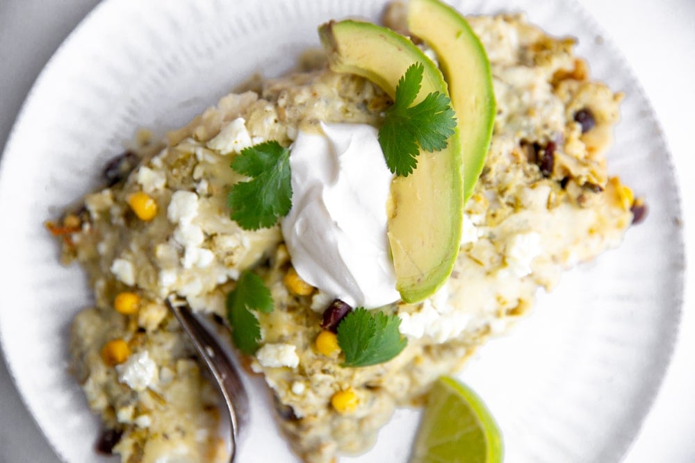 Close up of green salsa enchiladas on a plate, topped with sour cream and avocado. 