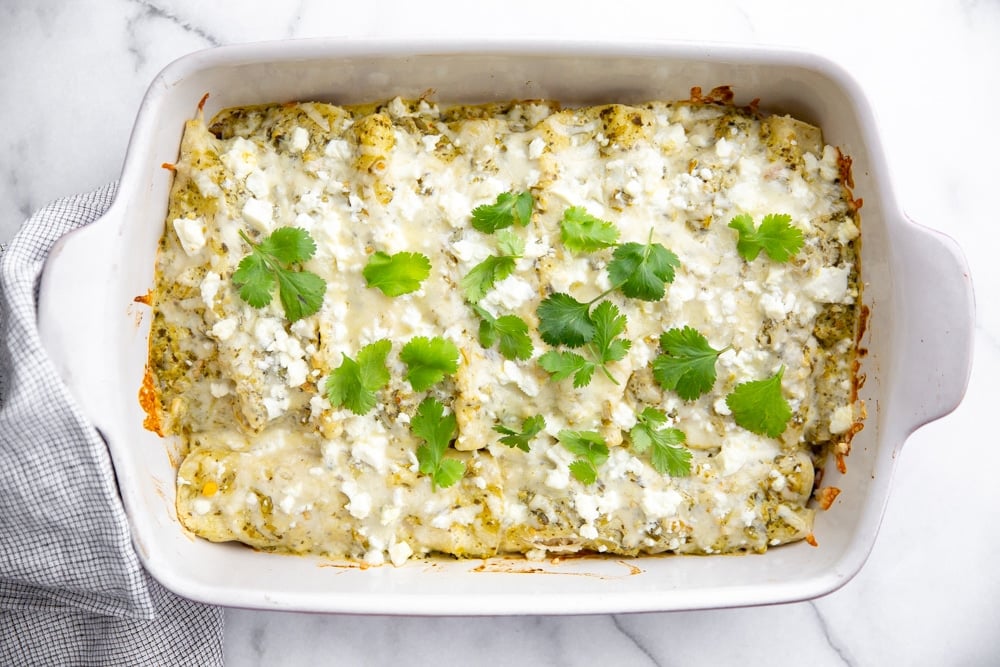 Green salsa enchiladas in a baking dish, sprinkled with cilantro. 