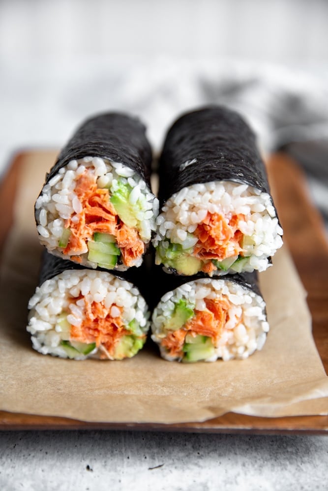 Spicy salmon sushi burrito rolls stacked on top of each other on a serving board. 