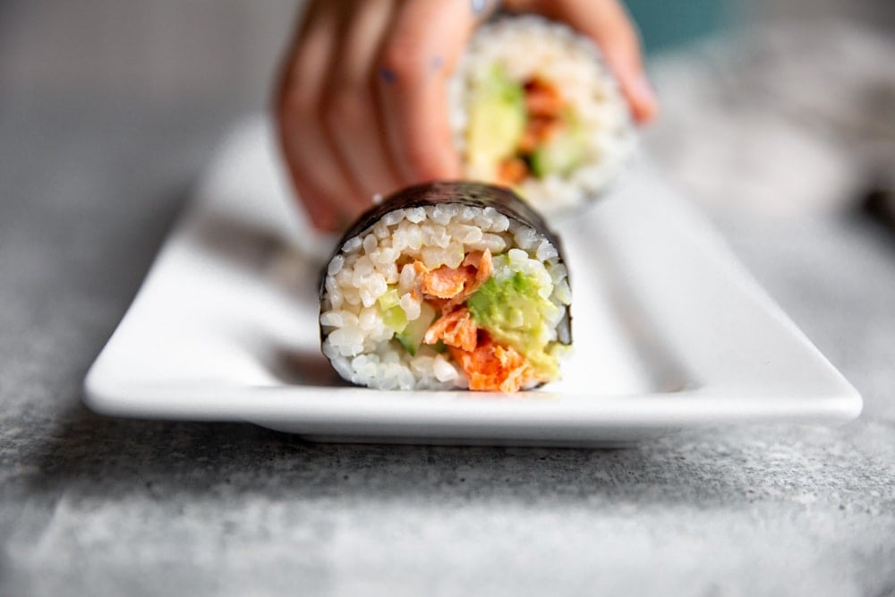 Hand grabbing a spicy salmon sushi roll. 
