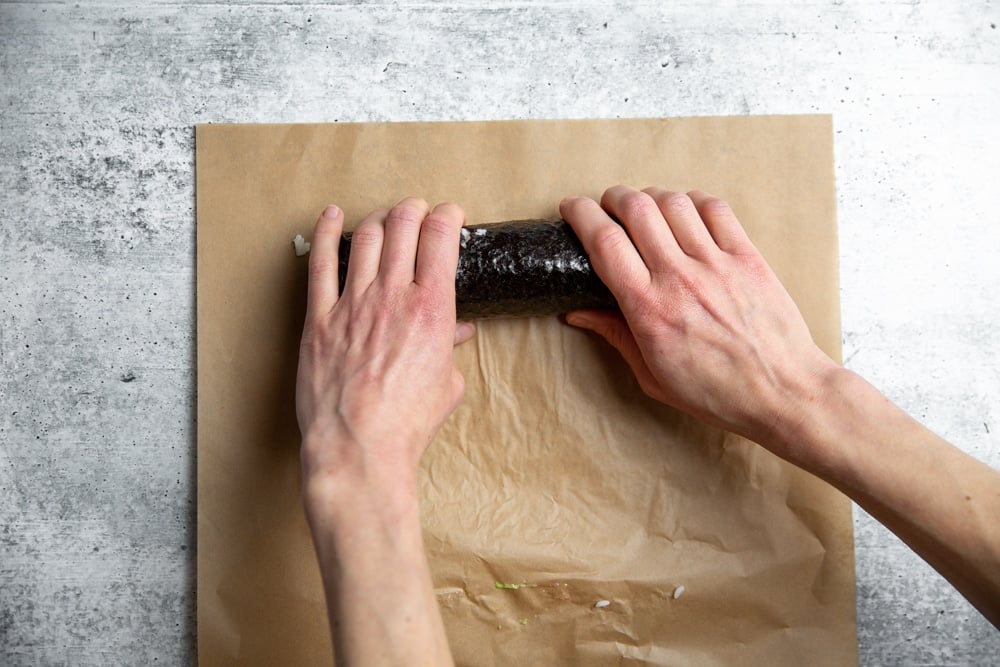 Hands rolling a spicy salmon sushi roll. 