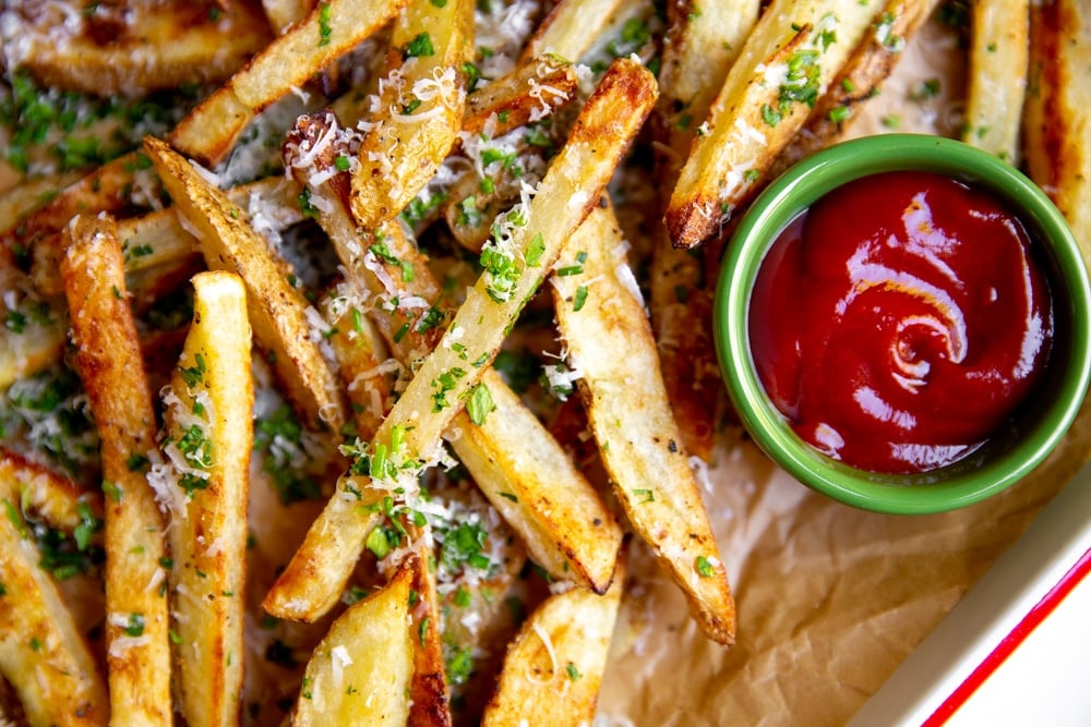 Herb baked French fries on a platter with a small bowl of ketchup alongside.