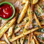Baked french fries with herbs and parmesan on parchment paper with ketchup.