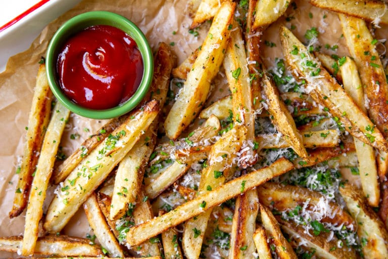 Baked french fries with herbs and parmesan on parchment paper with ketchup.
