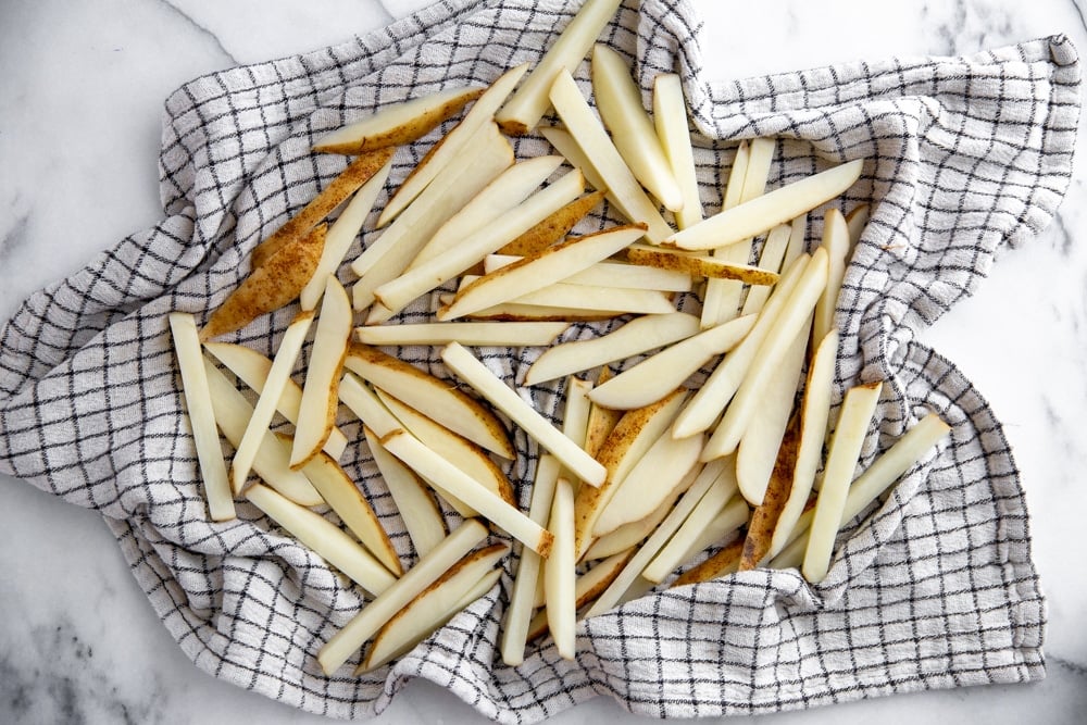 Process shot showing soaked French fries drying in a kitchen towel before baking. 