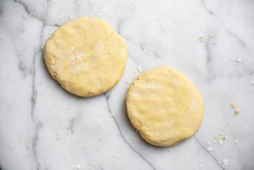 A batch of gluten free pie dough divided into two rounds on a marble surface.