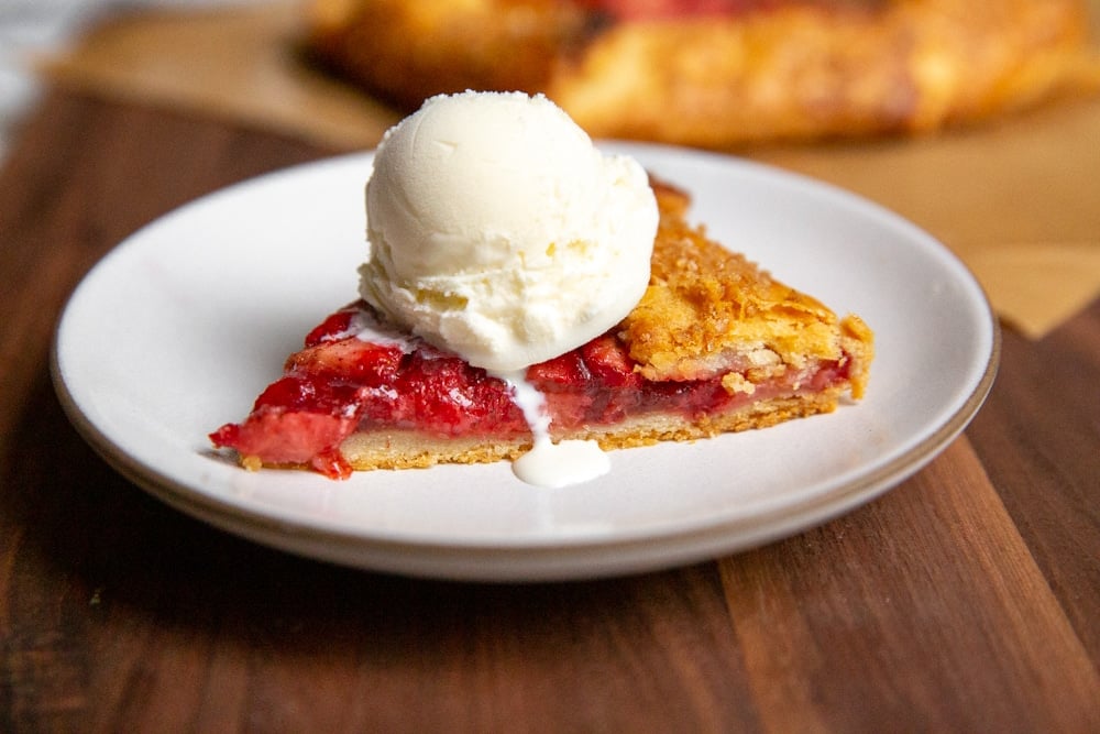 A slice of strawberry galette topped with a scoop of vanilla ice cream. 