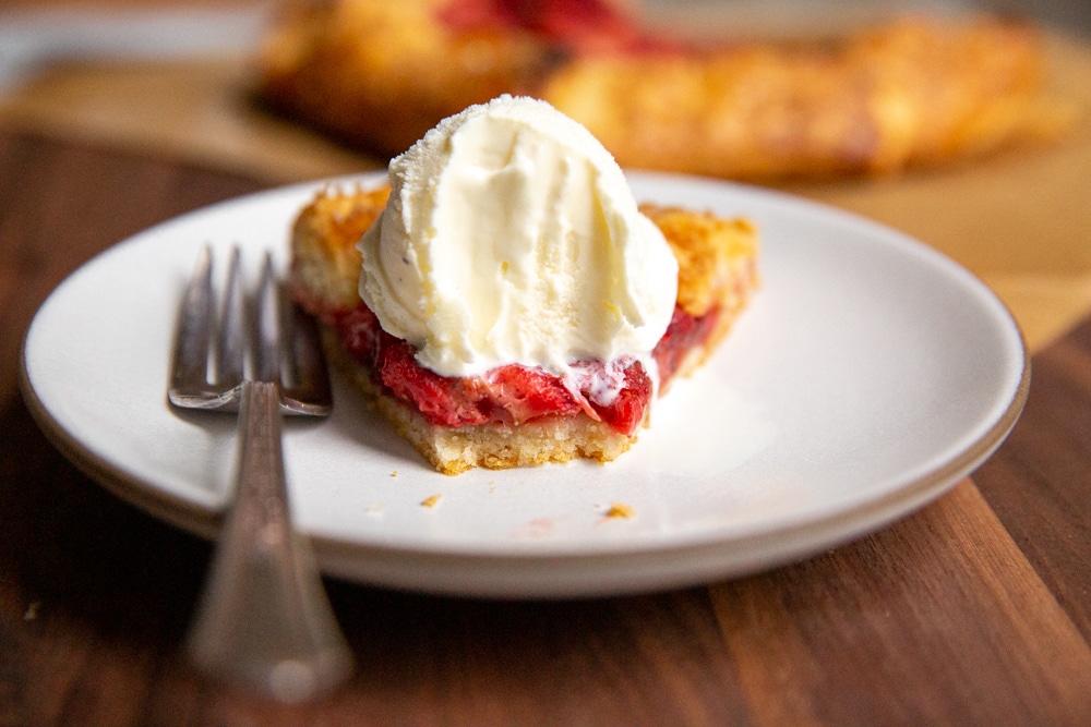 Slice of strawberry galette with ice cream on a plate with bite taken out. 