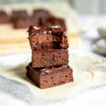 Three double chocolate zucchini brownies stacked on a piece of parchment paper.