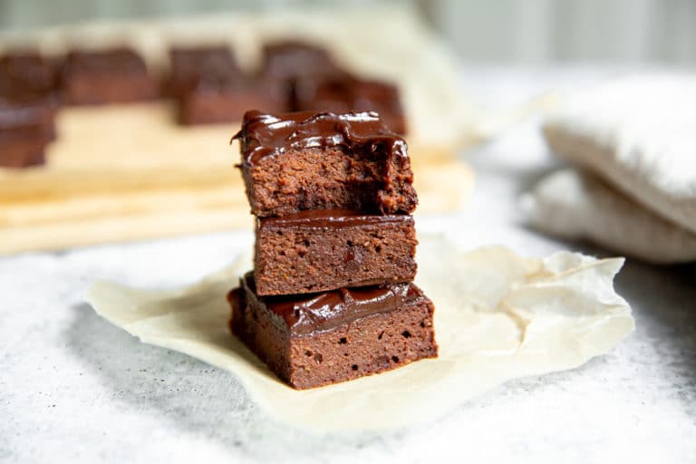 Three double chocolate zucchini brownies stacked on a piece of parchment paper.