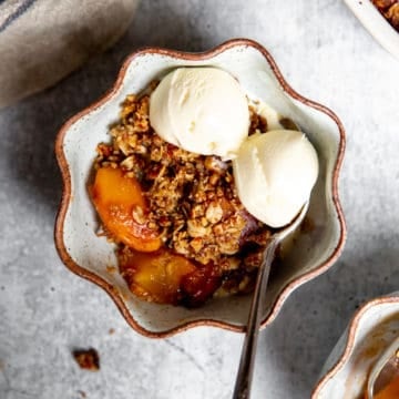 A serving of gluten free peach crisp in a bowl with a scoop of ice cream.