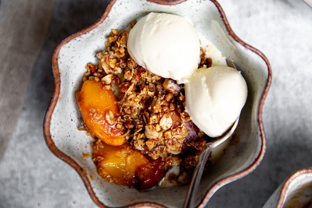 Peach crisp in a serving bowl, topped with vanilla ice cream. 