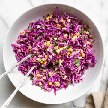 Red cabbage coleslaw in a bowl with serving spoons.