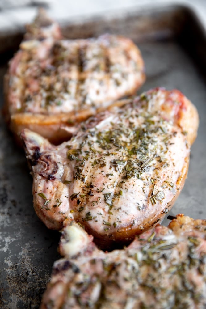 Grilled thick cut pork chops resting on a sheet tray. 