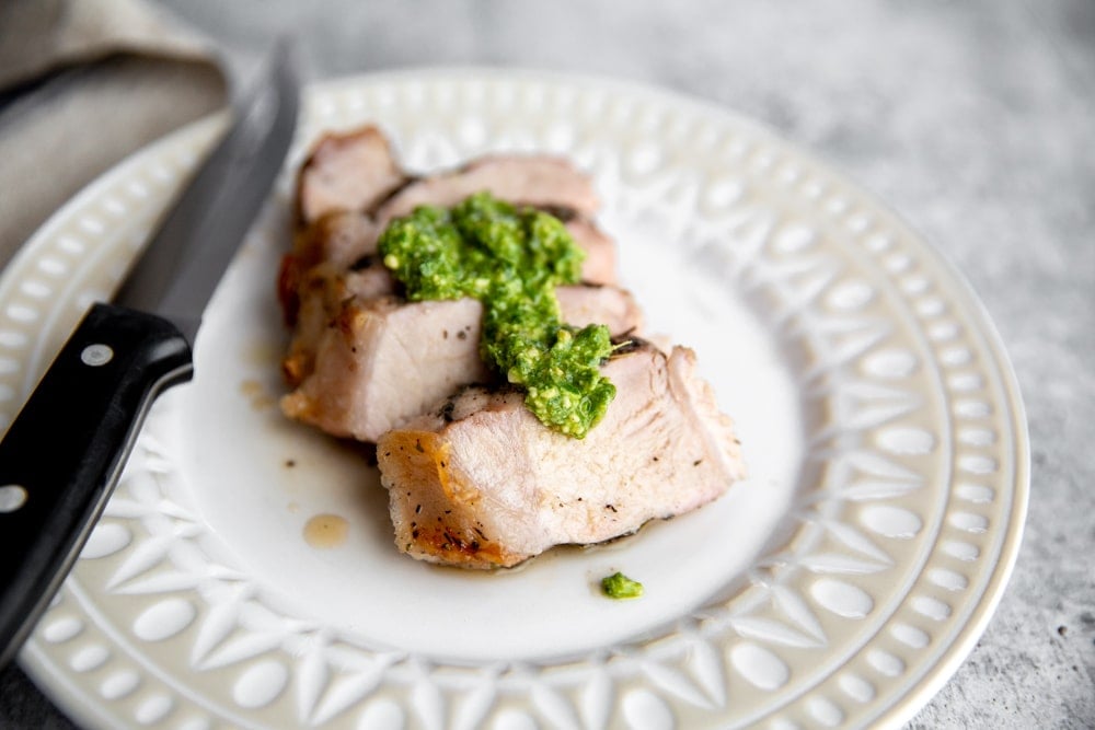 Grilled pork chop slices on a plate, topped with chimichurri sauce.