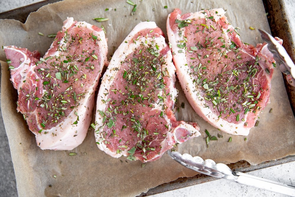 Process shot showing pork chops sprinkled with chopped herbs. 
