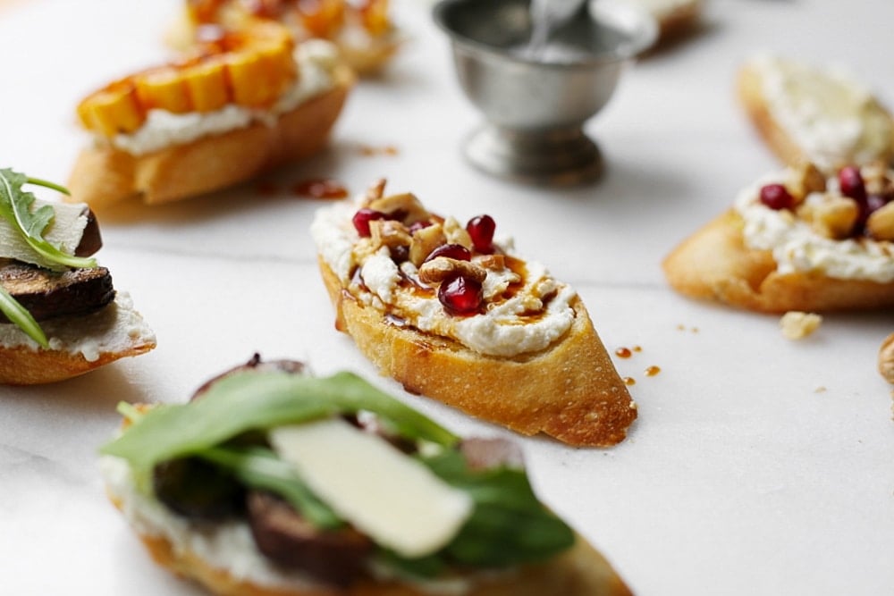 Whipped ricotta crostini topped with pomegranate seeds and walnuts on a marble surface.