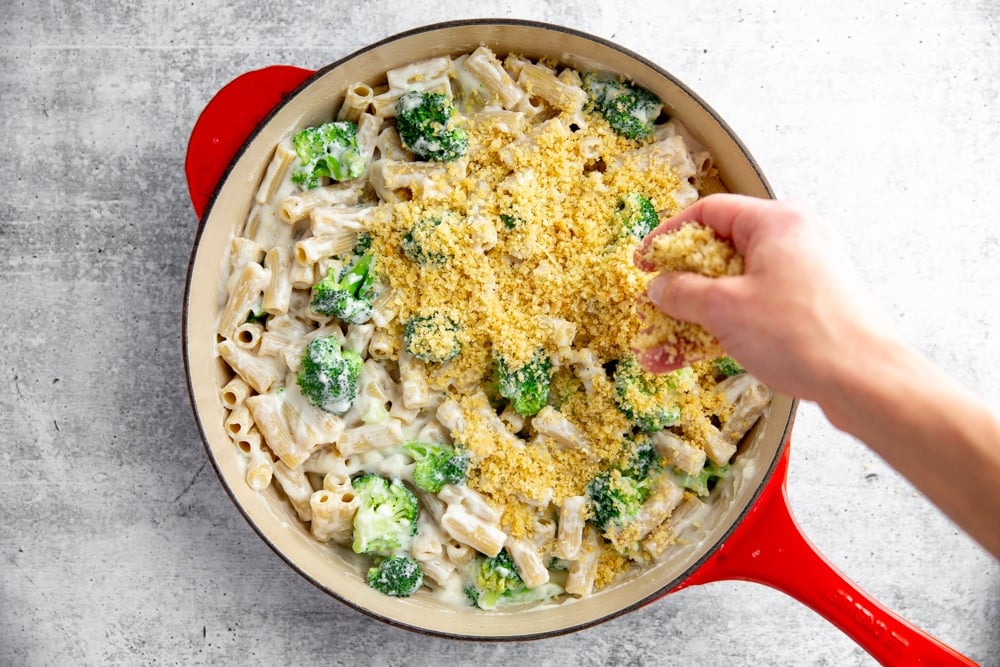 Hand sprinkling the breadcrumb topping over the broccoli pasta bake. 