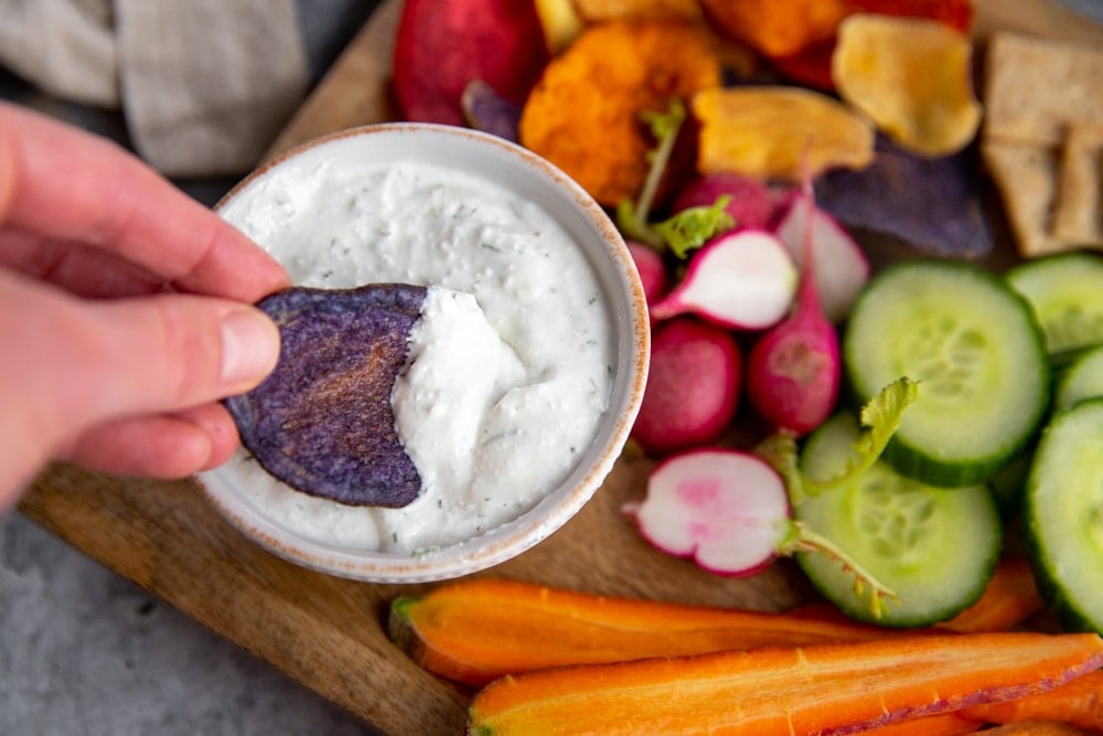 Hand dipping a purple potato chip into the healthy veggie dip.