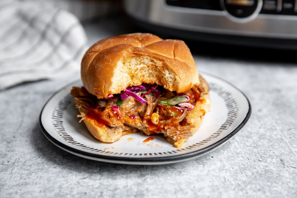 Close up of a slow cooker bbq pulled pork sandwich with a bite taken out.