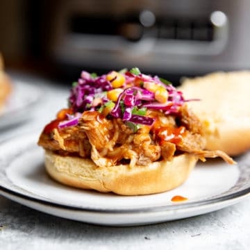 Slow cooker pulled pork piled on a bun, topped with coleslaw.