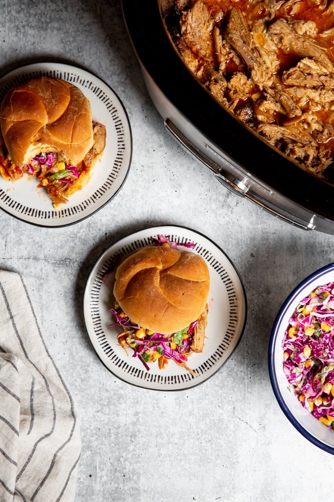 Overhead shot of a pulled pork in a slow cooker, with bbq pulled pork sandwiches alongside.